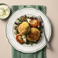 En tallrik med två risottobiffar, tomater, haricots verts och svamp står på en duk bredvid en skål med gremolata.