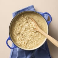 En gryta med risotto och en träsked står på en duk.