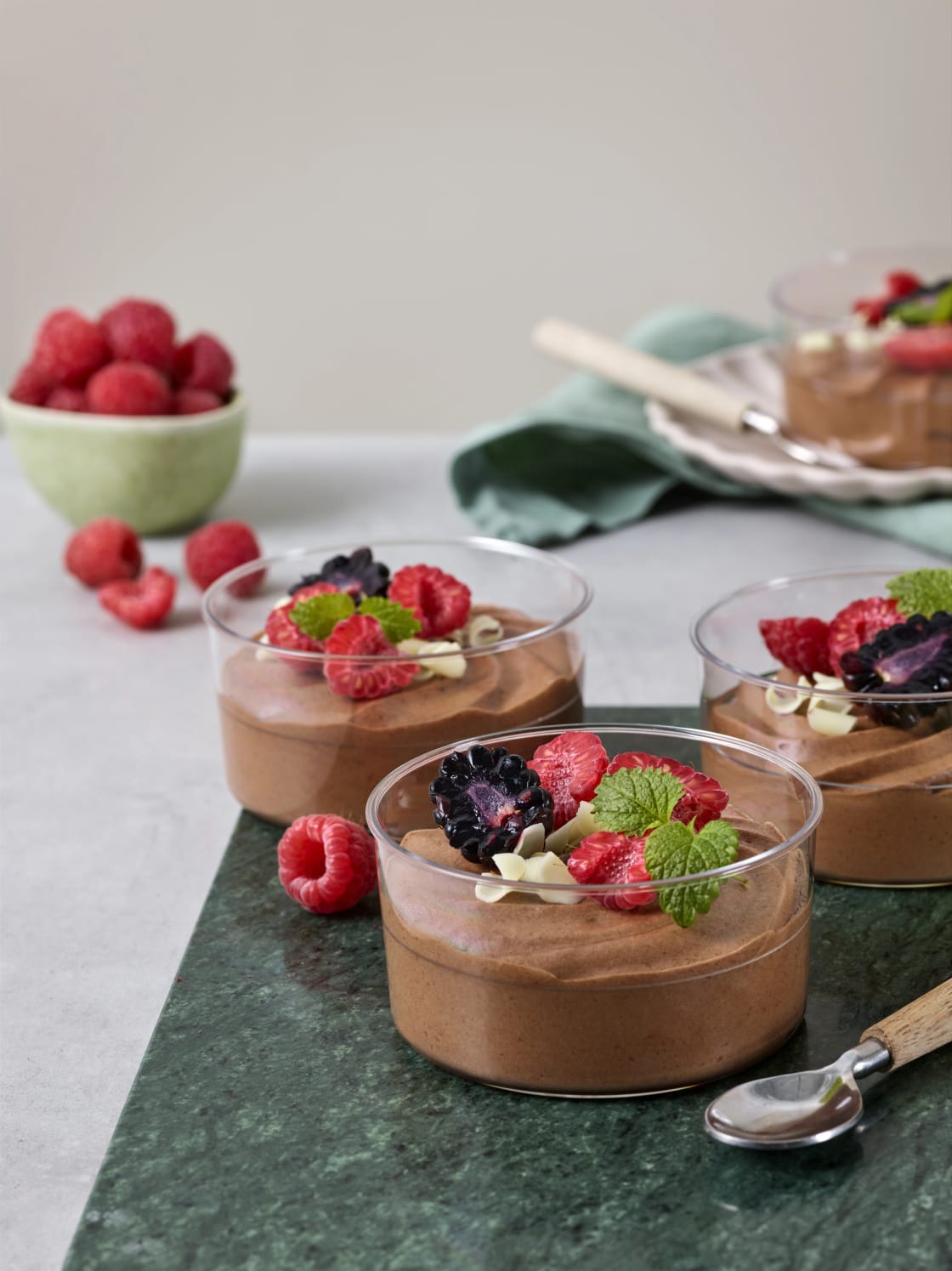 Tre portionsglas med chokladmousse dekorerade med bär och myntablad.