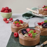 Tre glas med chokladmousse toppade med bär, chokladspån och myntablad.