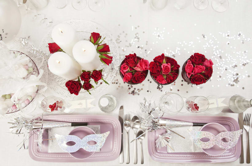 En klassisk dukning för fest och mottagning med vita dukar, kristall och inslag av silver. Röda, korta rosor som bryter av i två vaser mitt på bordet.