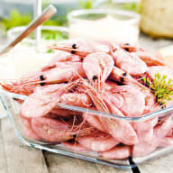 En skål med räkor står på ett bord tillsammans med bröd och grönsaker.