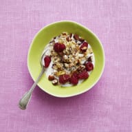 En skål med yoghurt, bär och müsli står på ett bord med en sked i.