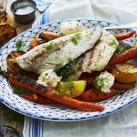 En tallrik med fiskfiléer, grillade grönsaker och örter står på en vit duk.