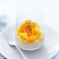 En glasskål med fruktsallad står på en vit tallrik med en gaffel bredvid.