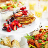 En tallrik med pannkakor och bär står på ett bord tillsammans med andra maträtter och drycker.