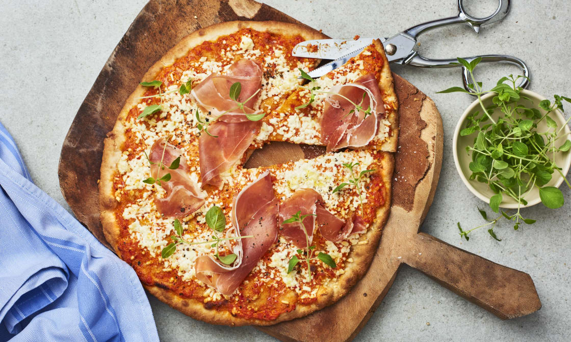 Nybakad pizza med skinka och örtdekoration på ett träunderlägg.