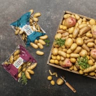En låda och två påsar med potatis ligger på en mörk yta.