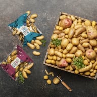 En låda och två påsar med potatis ligger på en mörk yta.