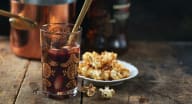 Ett glas med dryck och en sked står bredvid en skål med popcorn på ett träbord.