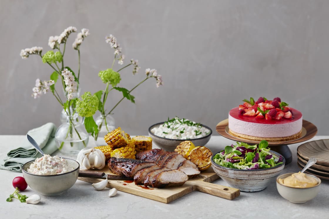 Skivor av grillat kött på en skärbräda i mitten av ett dukat bord med olika tillbehör.