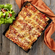 En lasagne i en form bredvid en sallad på ett träbord.