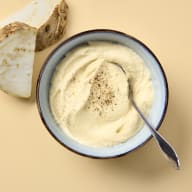 Rotsellerikräm i en skål med mald peppar på, bredvid skålen finns rå rotselleri.