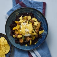En skål med svart ris, pulled pork och tomatsalsa med tortillachips står på ett underlag bredvid en vikt duk.