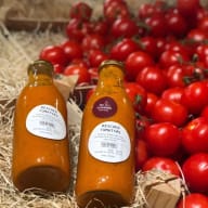 Tomater och flaskor med juice ligger på halm med en text ovanför bilden.