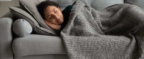 Bil på en kvinna som sover i soffan under en filt