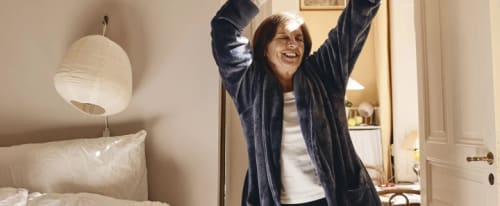 Jätteglad kvinna i morgonrock med händer ovanför huvudet.