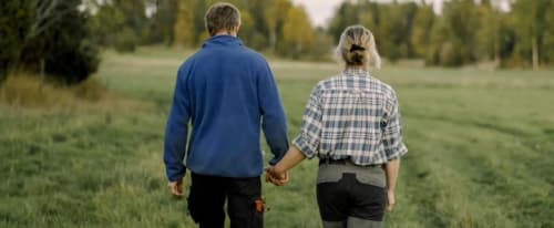 Man och en kvinna håller varnadras händer och går på ett fält från kameran.