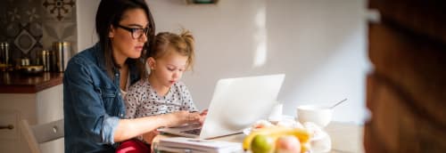 Mamma med barn vid köksbordet med laptop