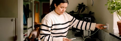 Tjej laddar mobilen vid köksbänken.