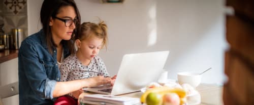 Mamma med barn vid köksbordet med laptop