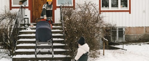 Kvinna som drar upp en barnvagn för en snötäckt trappa till ett hus.