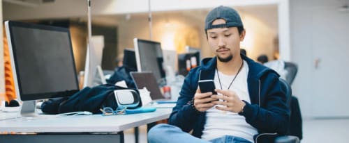 Ung cool kille sitter vid datorskärmar och tittar på mobilen.