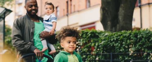 Man promenerar med en baby på armen och ett småbarn i vagnen.