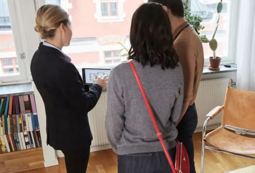 Mäklare visar en planlösning för ett par som tittar på en bostad.