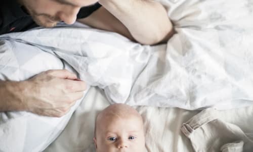 En pappa ligger i en säng och tittar på en bebis.