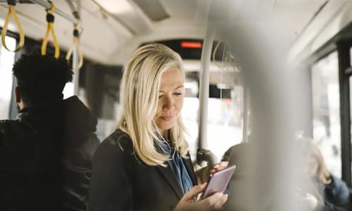 Kvinna som står i en buss och tittar på sin mobiltelefon.