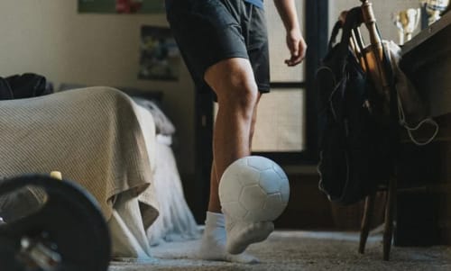 Kill i ett pojkrum som balanserar en fotboll på foten.