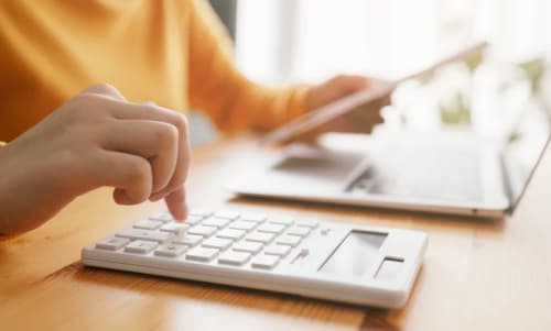 Person som sitter framför en dator och räknar på en miniräknare.