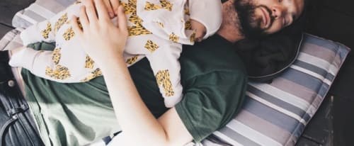 Pappa som sover med sin baby på bröstet.