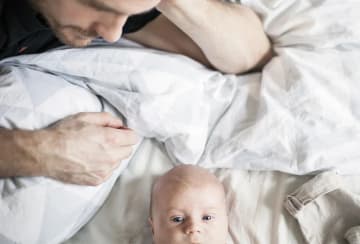 Pappa ligger på sängen och tittar på sin baby 