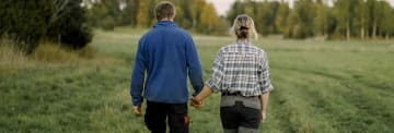 Man och en kvinna håller varnadras händer och går på ett fält från kameran.
