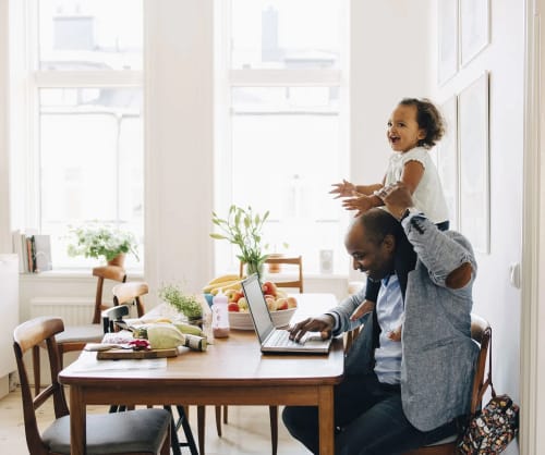 Pappa vid en dator med dottern på axlarna.