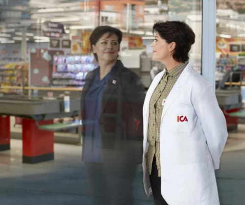 ICA-handlare som tittar mot sin refelktion i ett butiksfönster. Mans er även kassorna i butiken refleteras.