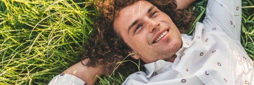 Man ligger i gräset och tittar upp mot himlen. Mest köpta fonder hos ICA Banken.