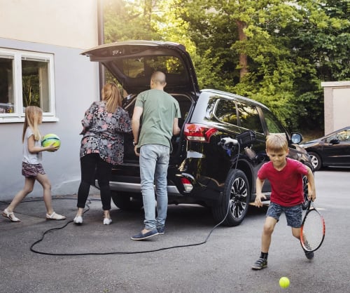 Familj som packar elbilen som står på laddning utanför huset. Låna till köp av elbil hos ICA Banken.