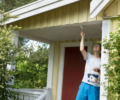 En man målar om huset. Hos ICA Banken kan du ta ett renoveringslån för dina projekt.