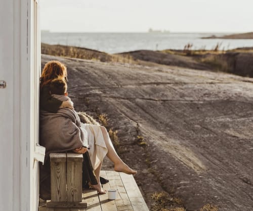 Mamma och barn sitter och tittar ut över havet. Månadsspara till dina drömmar hos ICA Banken.