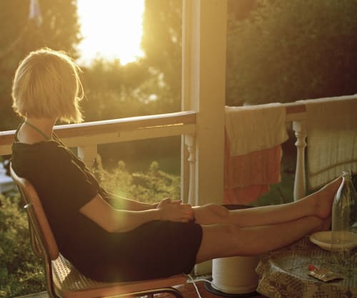 Kvinna som sitter på verandan och tittar mot solnedgången. Spara till dina drömma i någon av ICA Bankens egna fonder.