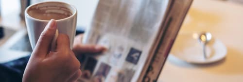Person dircker kaffe och läser tidningen.