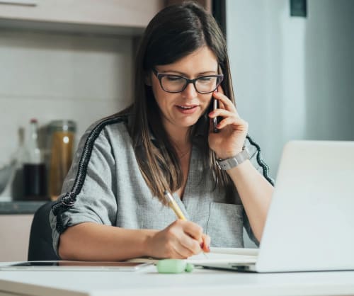 Kvinna framför en dator som talar i telefon. Boka möte om bolån och din ekonomi.