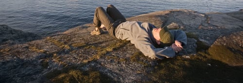 En man vilar i solen på en klippa vid havet.
