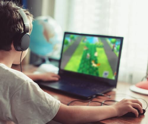 Barn som spelar datorspel på en dator. Bedrägerier mot unga är nåogt som ökar.