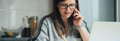 Kvinna pratar i telefon vid sin laptop i köket