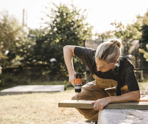 Kvinna borrar i en planka i trädgården.
