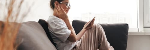 Kvinna kollar på mobilen sittandes i soffan.